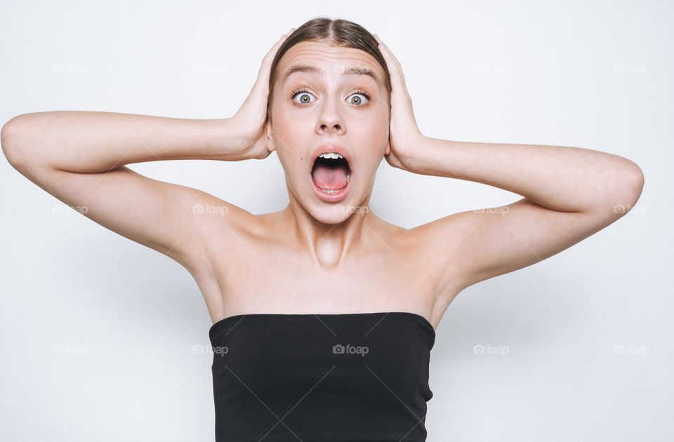 Portrait of surprised upset teenage girl frowns with hands near face on white background isolated