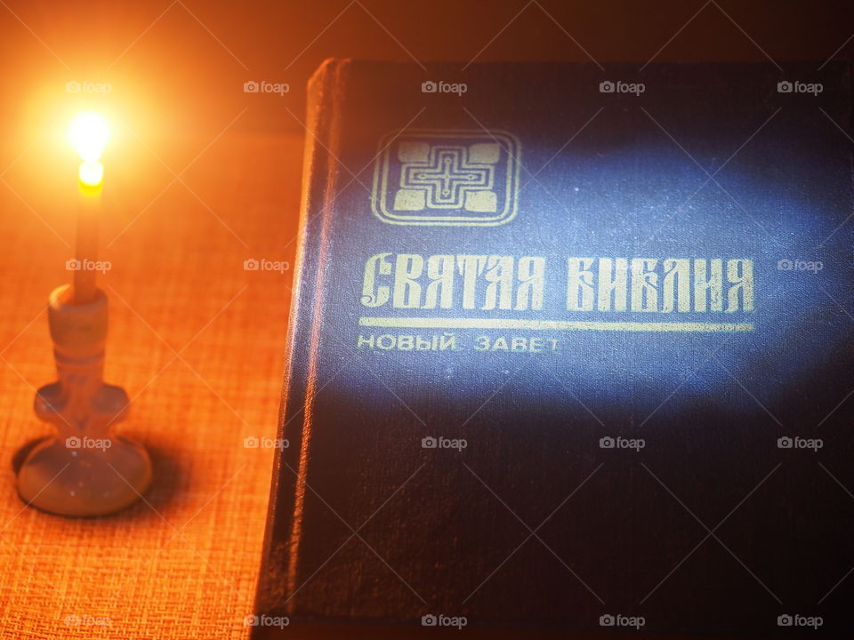 The Bible lies on a table and a burning candle stands