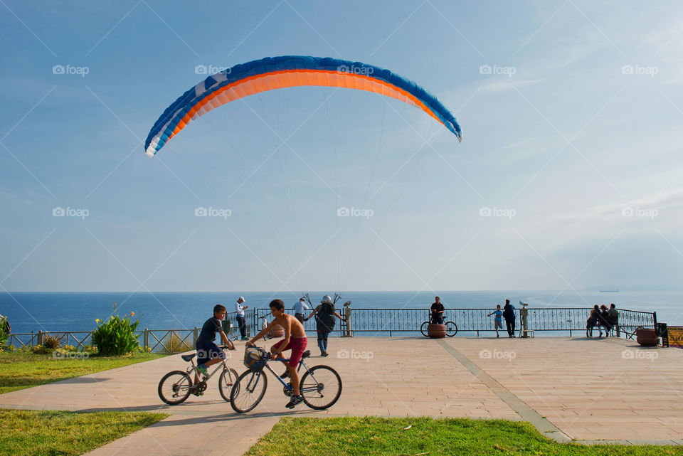 two teenagers on the bicycles a and the man with parachute on the Mediterranean Sea background