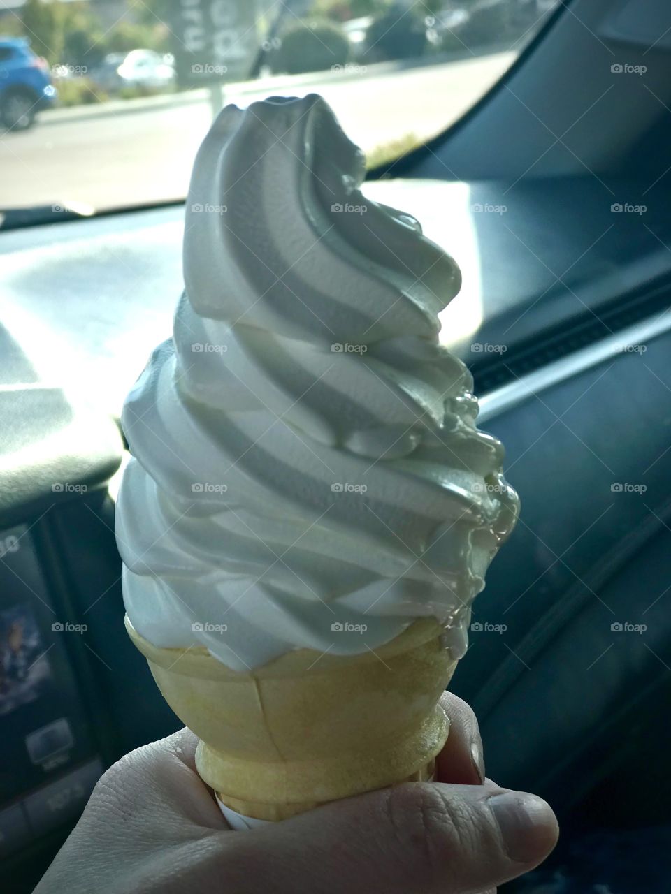 Holding a vanilla ice cream cone in the car while on a road trip vacation 
