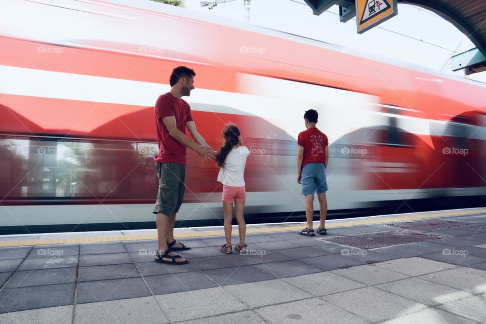 Fast train crossing at the station. Kids looking. Little girl put her hands on her ears