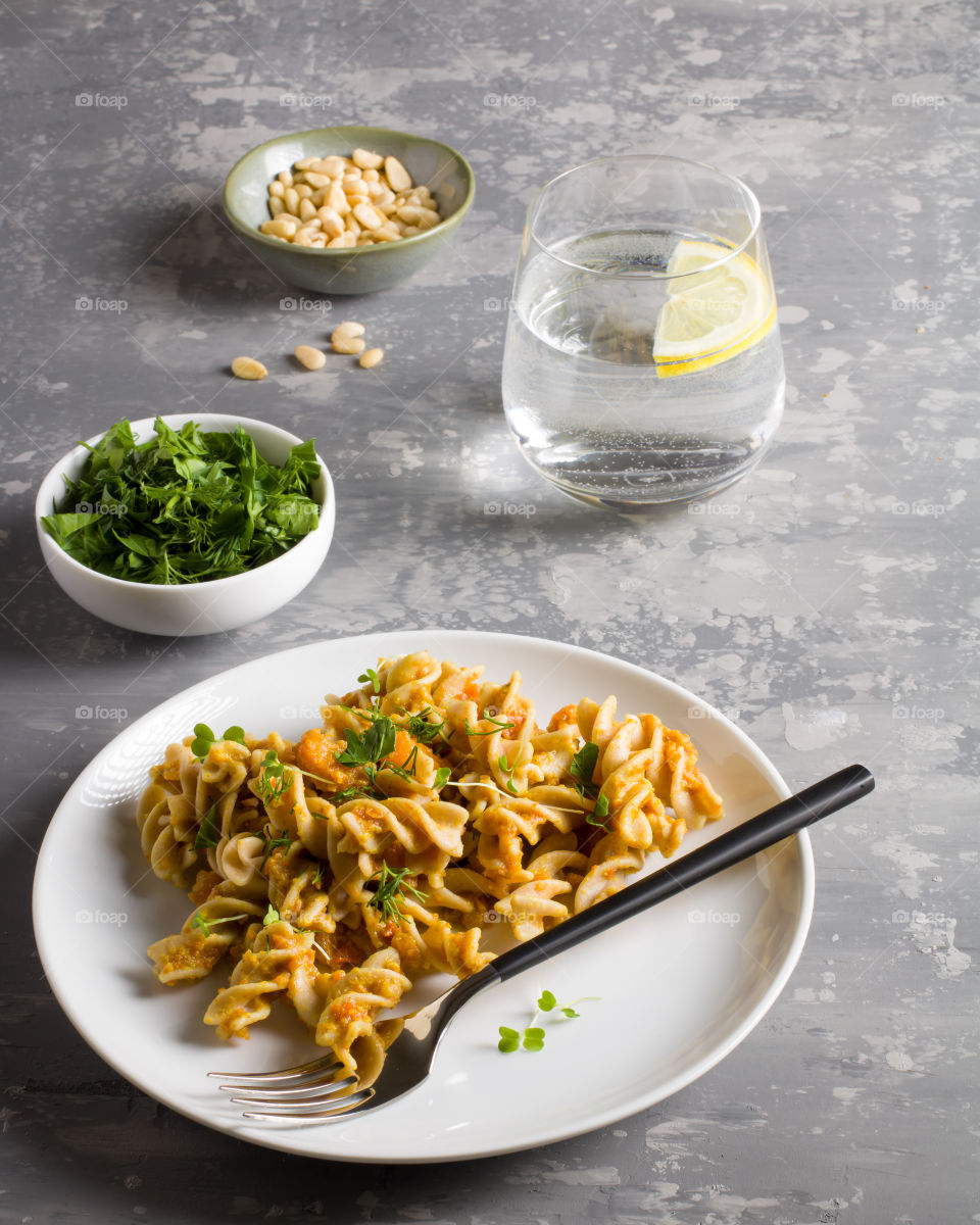 Pasta with curry sauce, served with greens and a glass of water on the grey table