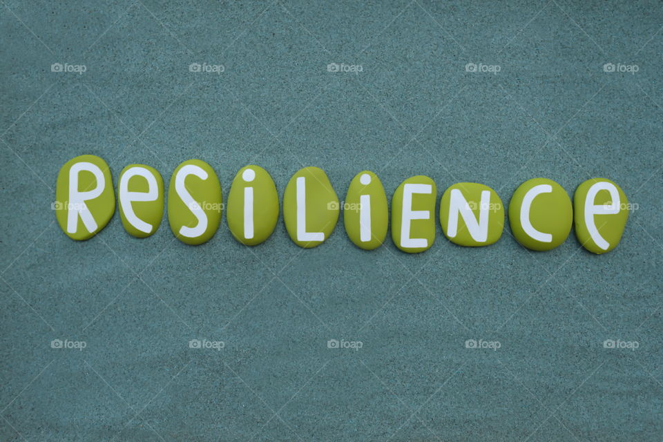 Resilience word composed with green handmade painted stone letters over green sand