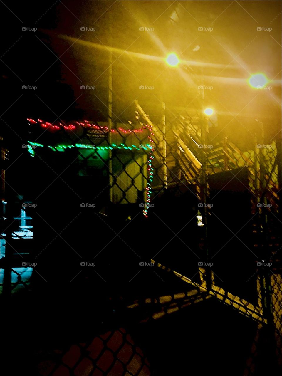 This is the parking lot beneath the „Pulaski Bridge“ at „Newtown Creek“ in LIC, Queens. For a while a food vendor had his shop set up there with its own festive lighting to show the way. 2021. Hypnotic Productions
