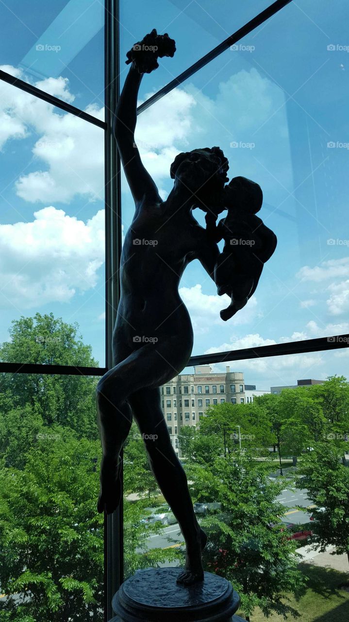 Statue of an old woman dances with a baby while overlooking a city garden.