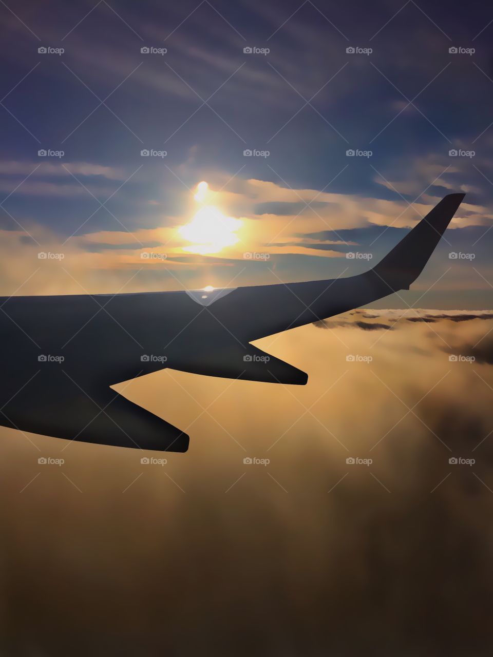 Aerial sunset from space viewed through the window of a jet airplane flying in the clouds.