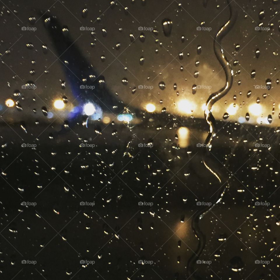 Rain falling on plane window at Atlanta airport at dusk with reflections.