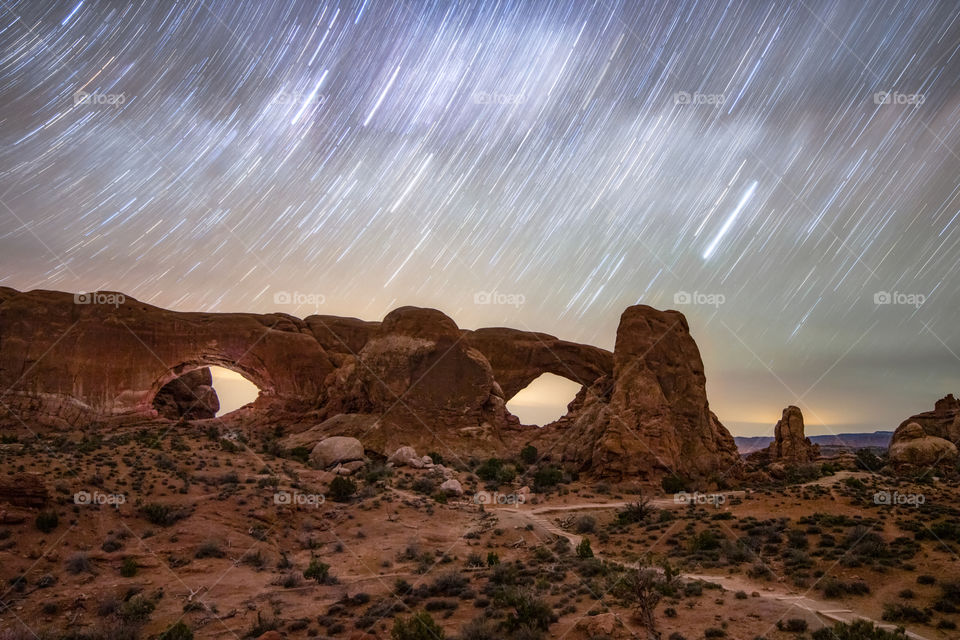 Star trails streaking across the night sky over natural sandstone arches in Arches National Park near Moab Utah. 