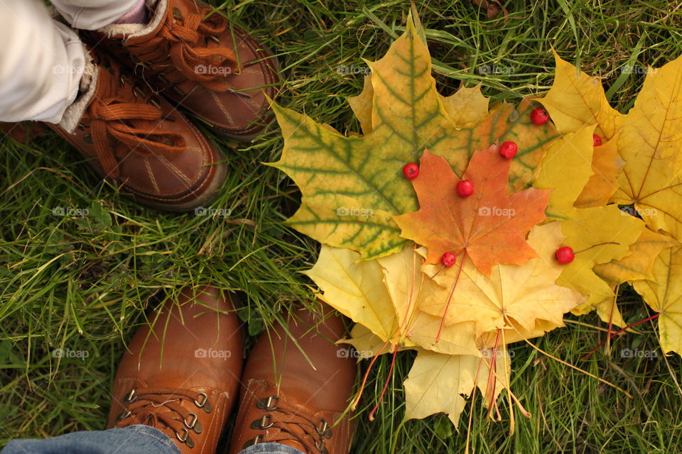 Selfie photo of feet in the autumn shoes of mom and daughter with harvested maple leaves and hawthorn berries