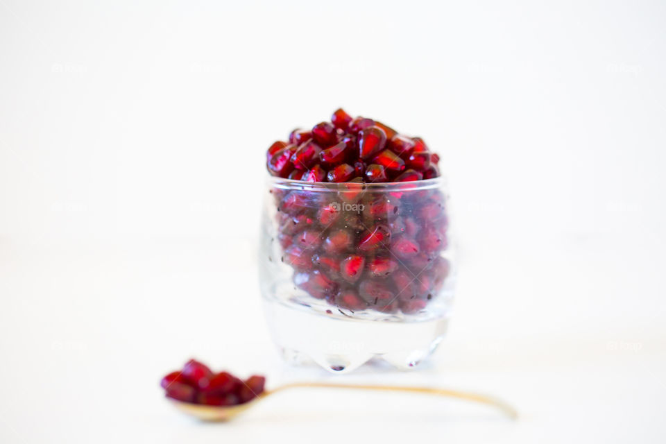 Fresh pomegranate seeds in a glass with a spoon on a white background. Fresh summer healthy fruit. Delicious and juicy red fruits.
