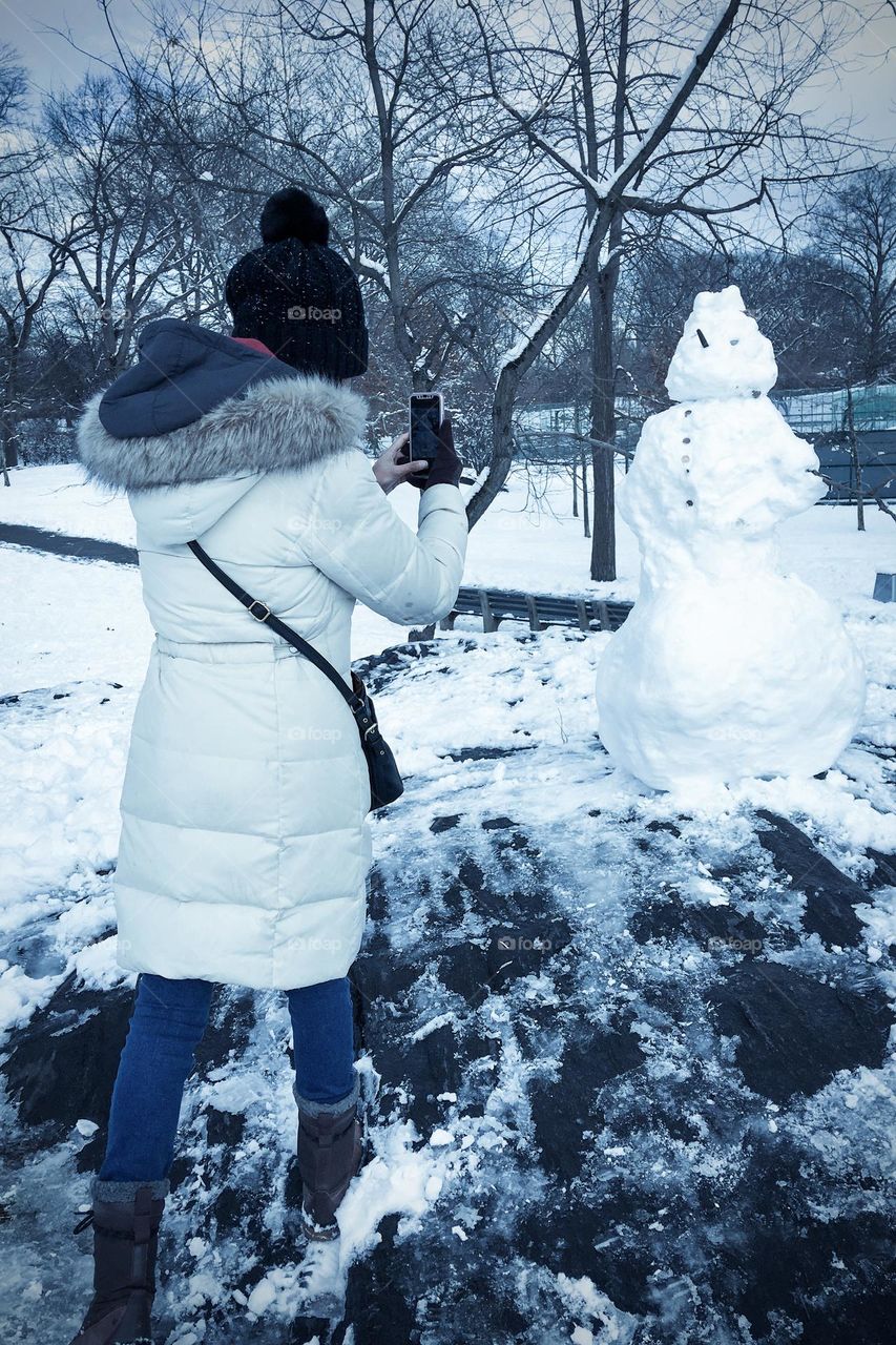 A woman taking picture of a snowman 
