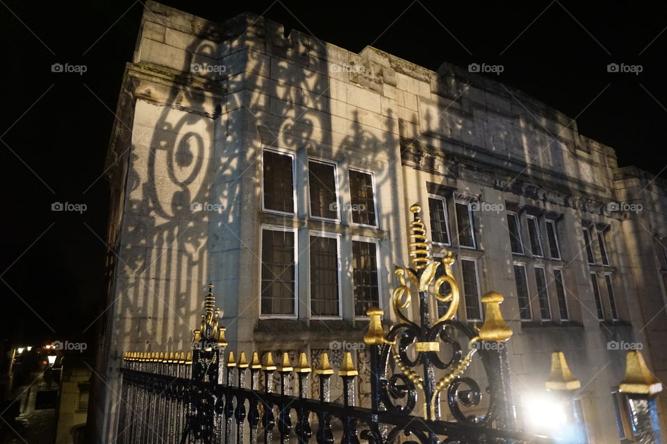 Building lit up by street lighting casting shadows of the fence on the facade 