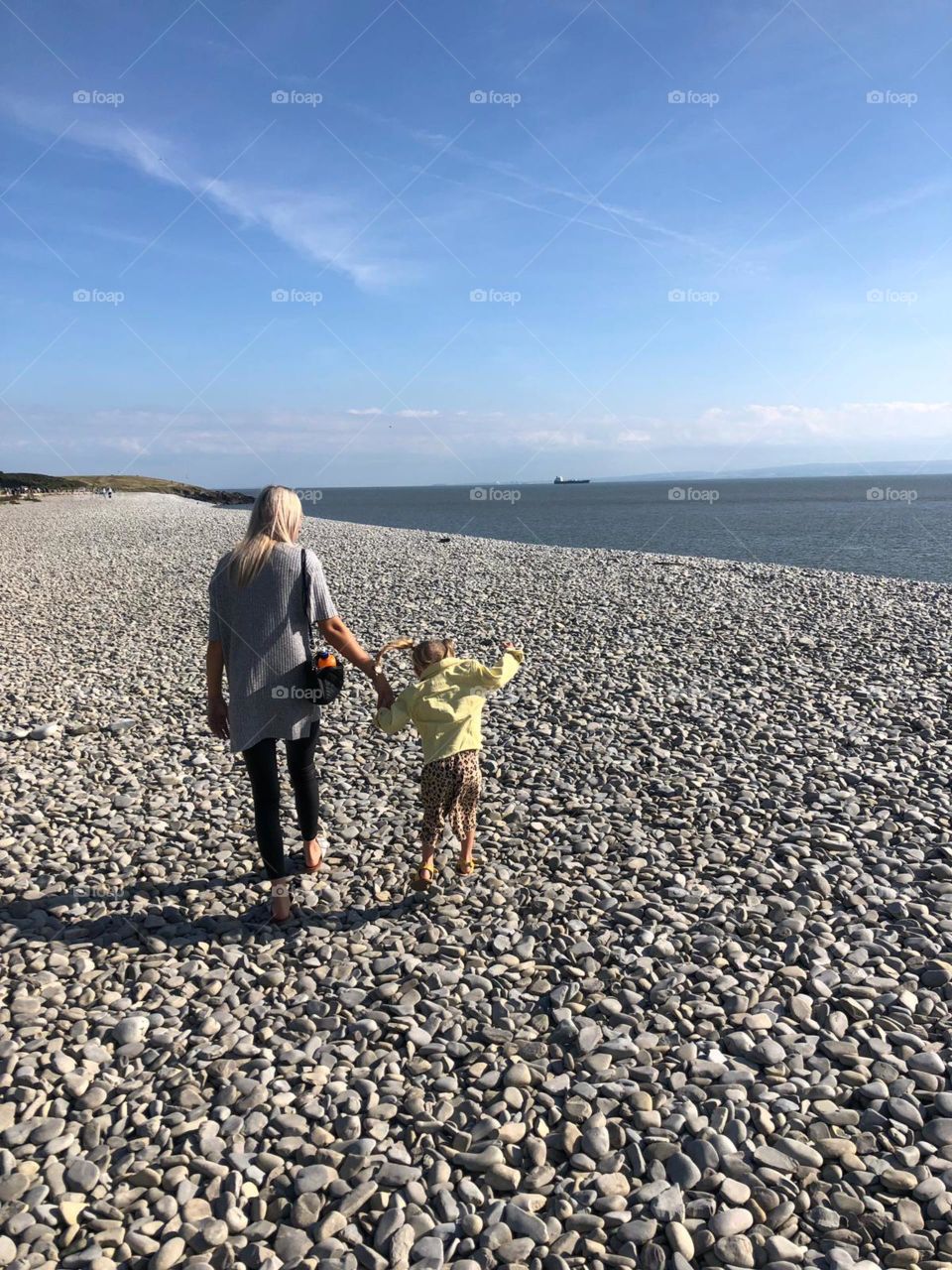 Mum and daughter walking on pebble beach 
