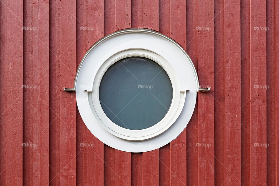 Round white window on red wooden house facade 