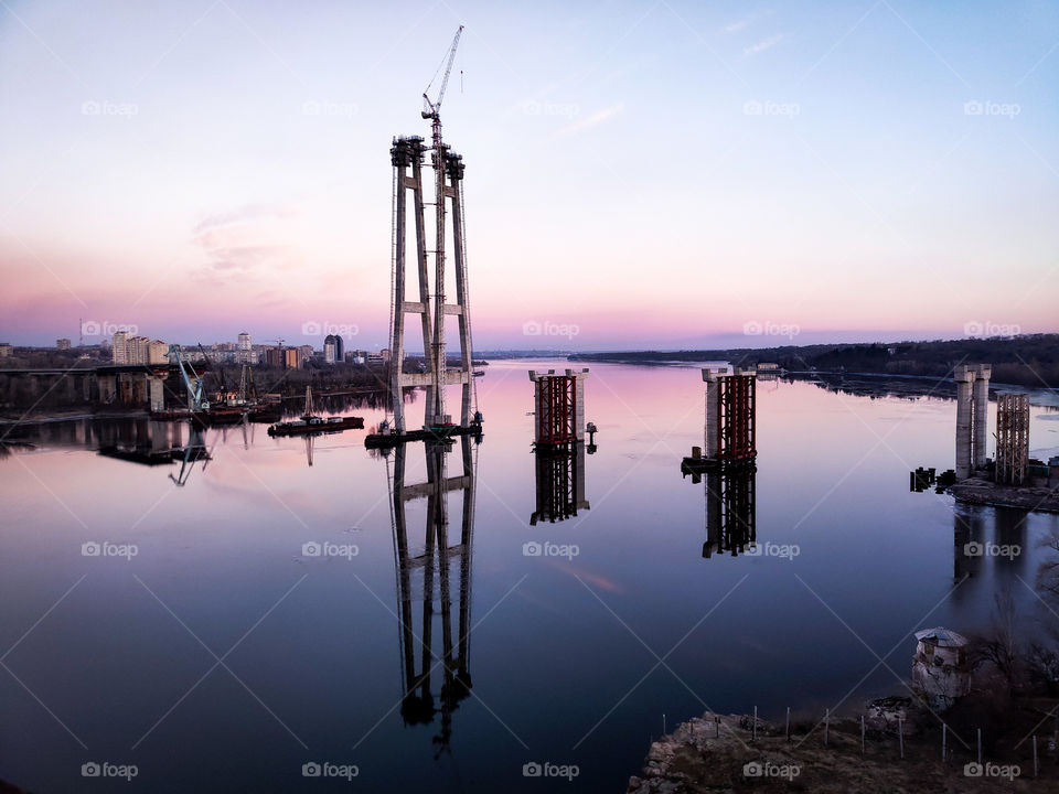 View on the unfinished bridge in Zaporozhye, Ukraine. Reflection in the water. Purple sunset.