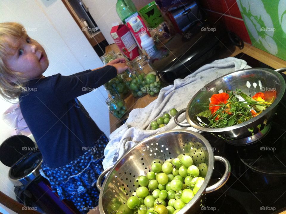 A little girl preserving green tomatoes in jar at kitchen