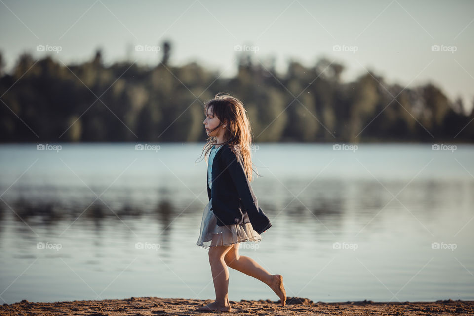 Little girl on lake coast at sunny evening. 