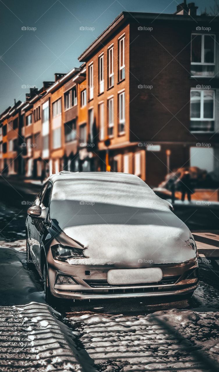 One snow-covered car is parked on the side of the road in the city of Brussels in Belgium, close-up side view.