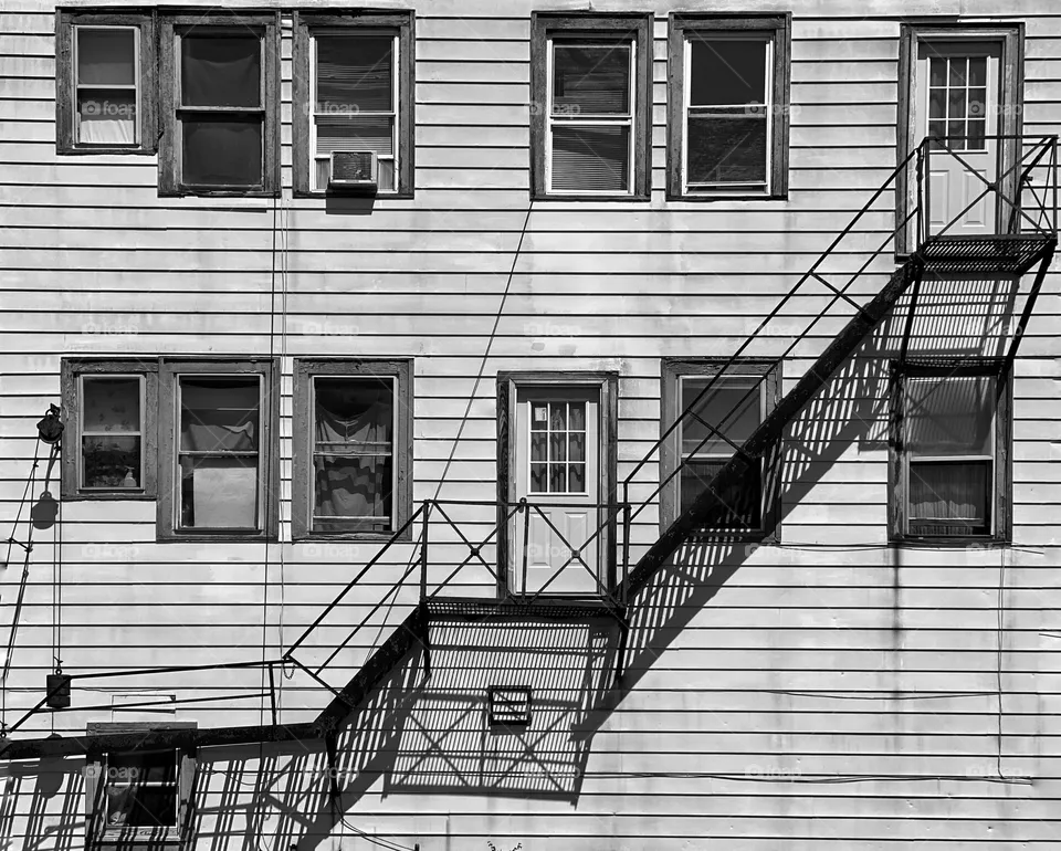 Fire escape and its shadow on the side of a wooden building 