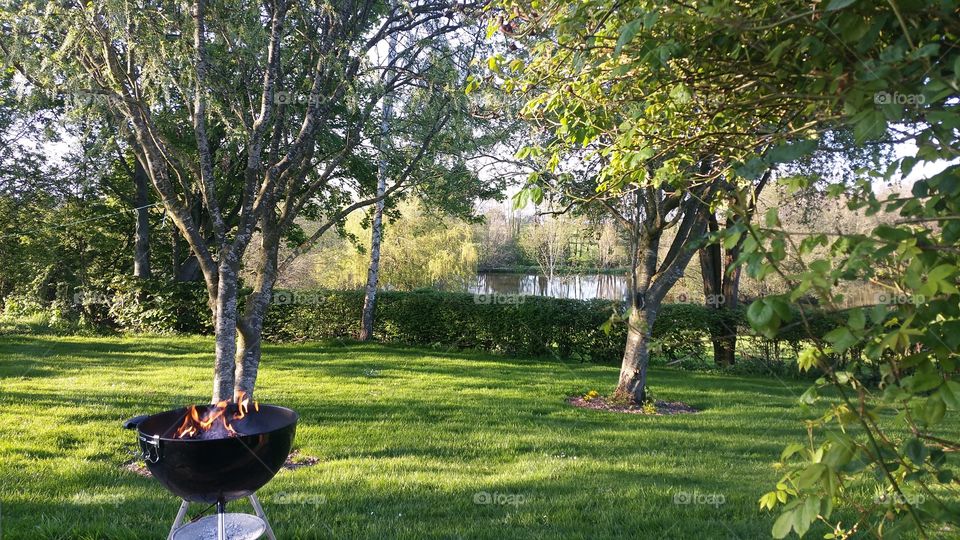A BBQ lit in a beautiful green garden over looking a lake on a sunny summers afternoon.