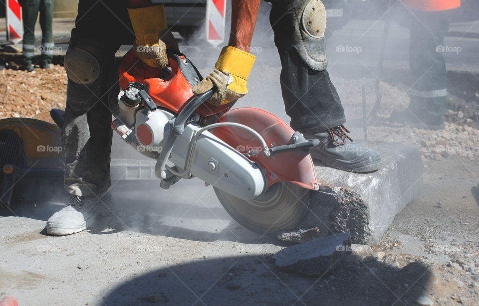 Builder worker with cutt-off machine power tool breaking concrete at road construction site