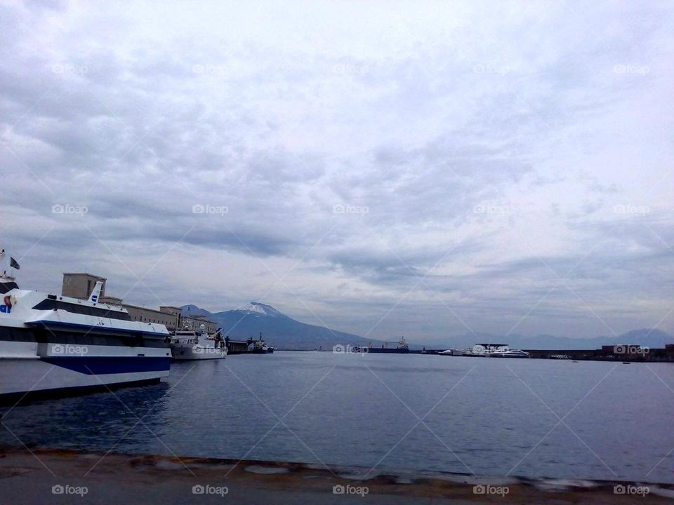 Beverello hydrophoil terminal in the port of Naples with Mount Vesuvio covered with snow in a cloudy winter day