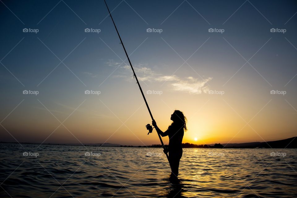silhouette of girl fishing at sunset