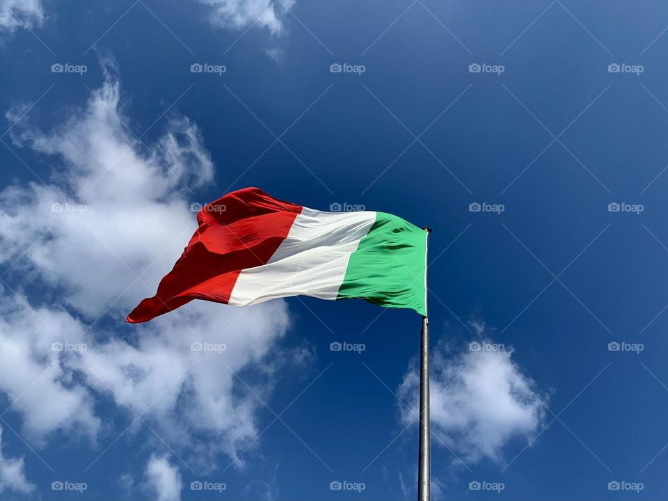 the Italian flag flutters against the blue background of a clear sky