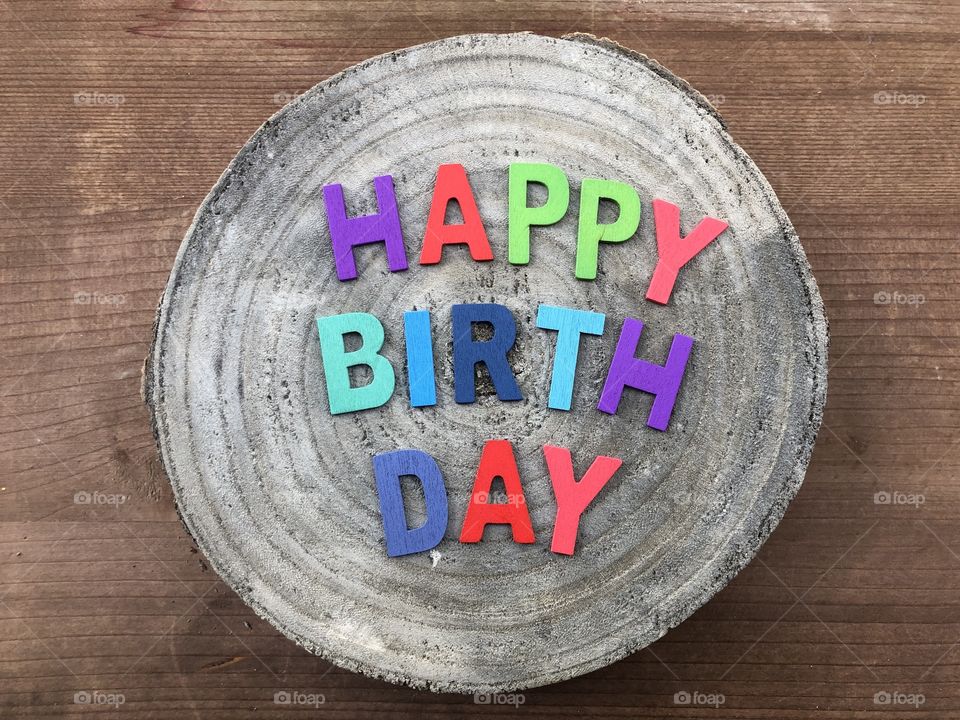 Happy Birthday text with colored wooden letters over a wooden mango round piece