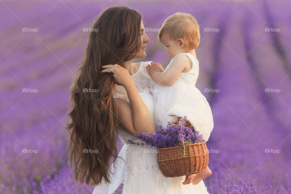 Beautiful woman with little girl 1-2 years old walking in lavender field 