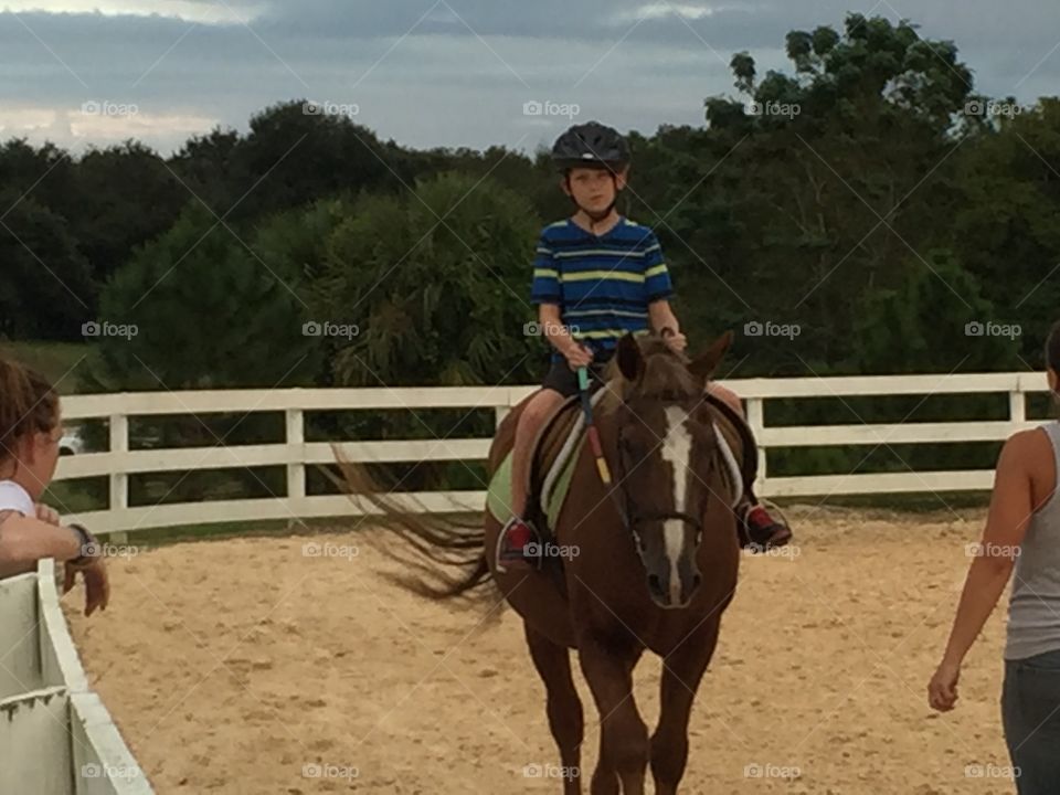 A little boy with helmet on horse at farm