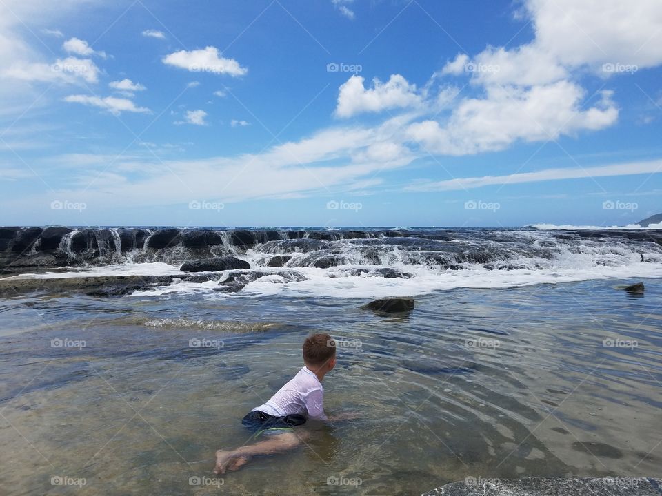 Boy plays in tidal pools as waves crash in