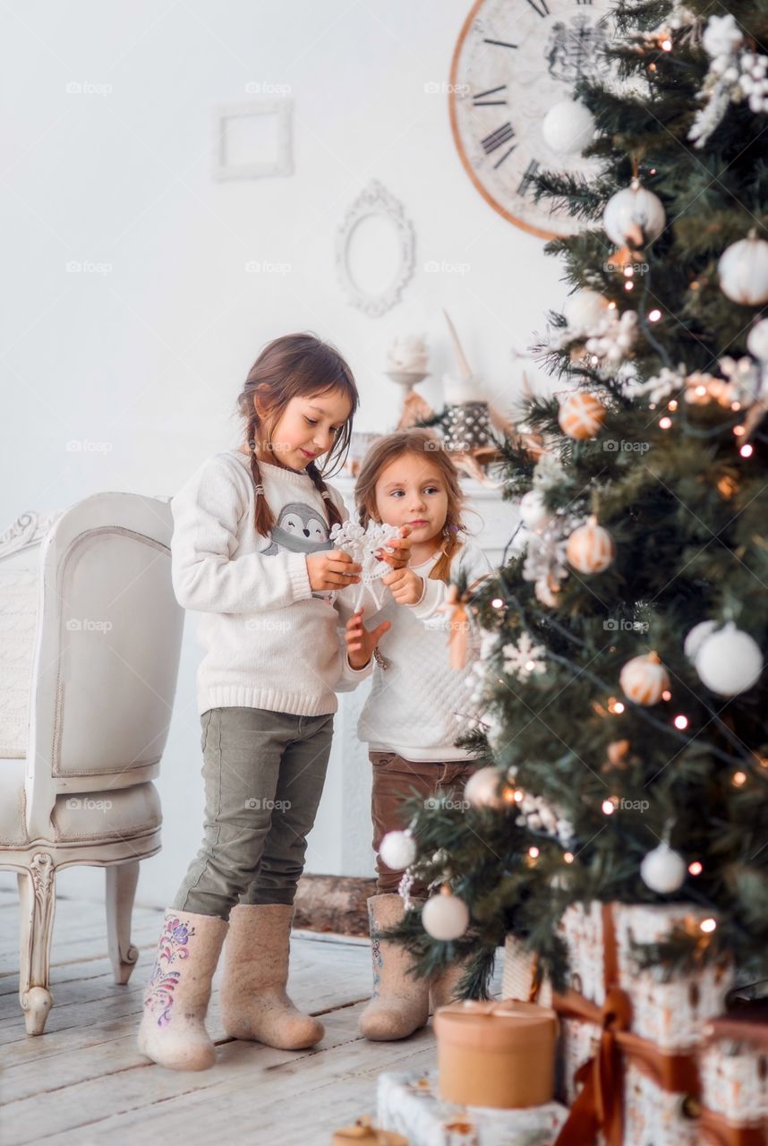 Little sisters near Christmas tree at home