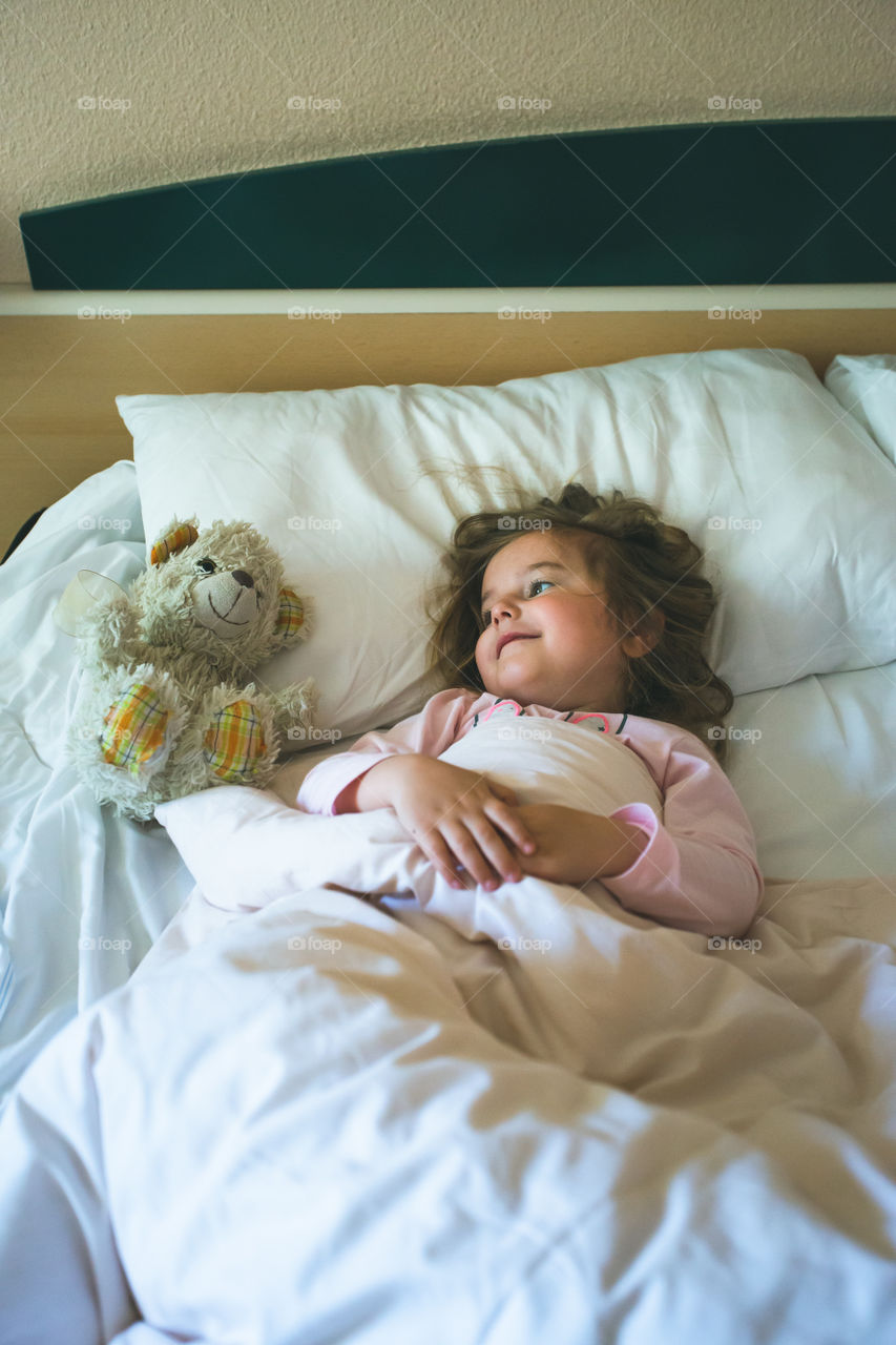 Little girl lying in a bed with teddy bear at the morning