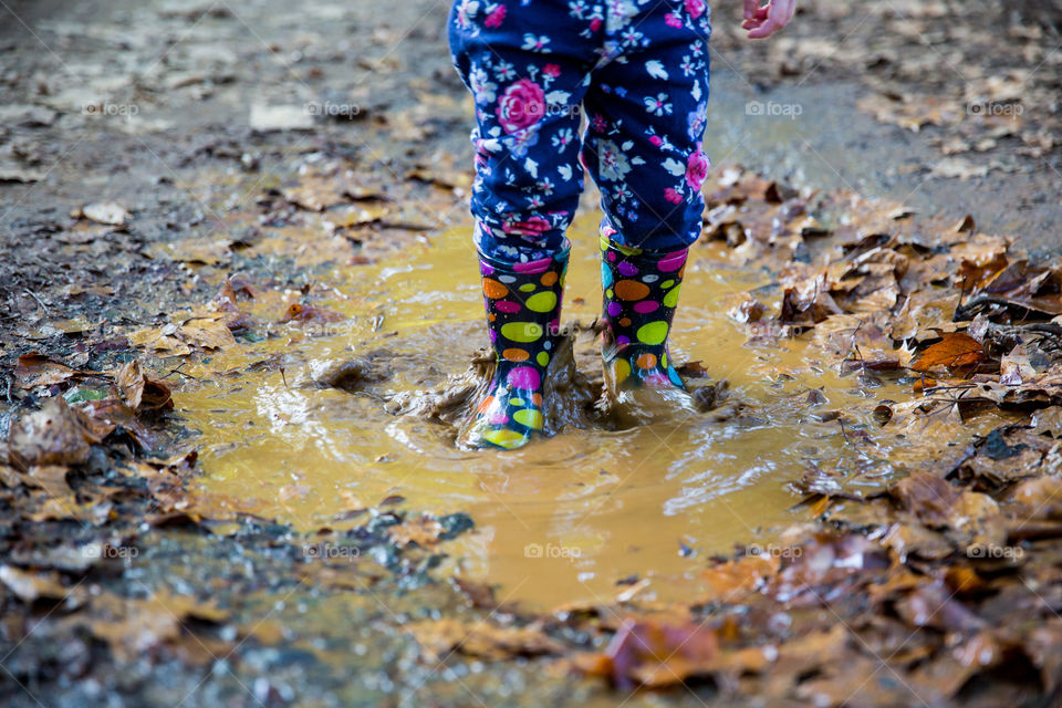 Little girl playing with colorful boots in mud after the summer rains. Summer time is a time to play and have fun outdoors, to enjoy the rain and thunderstorms. Little girl having fun with mud and water.