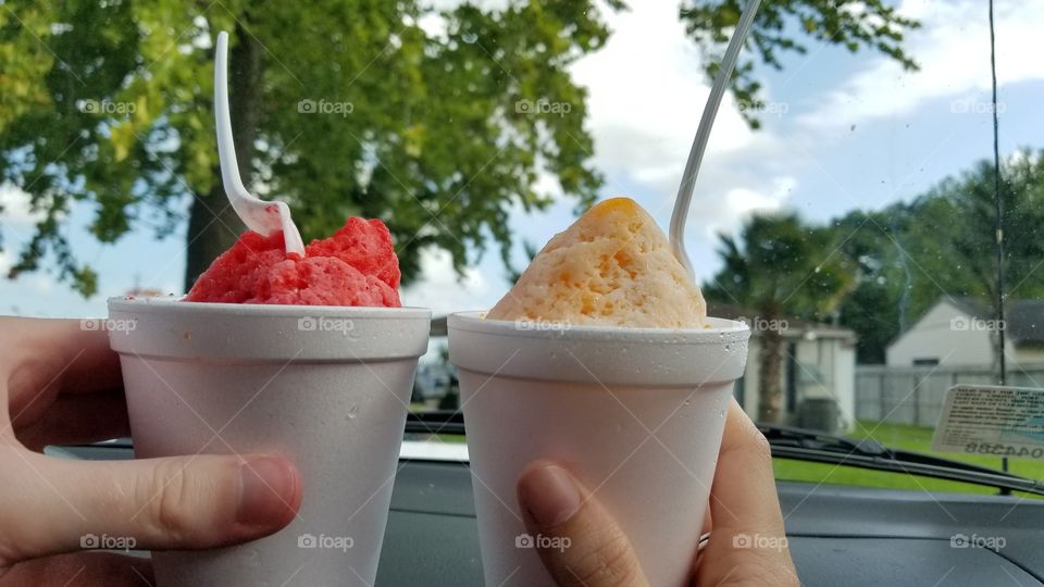 A strawberry cheesecake snowcone cheering with a dream sicle snowcone on a hot summer day.