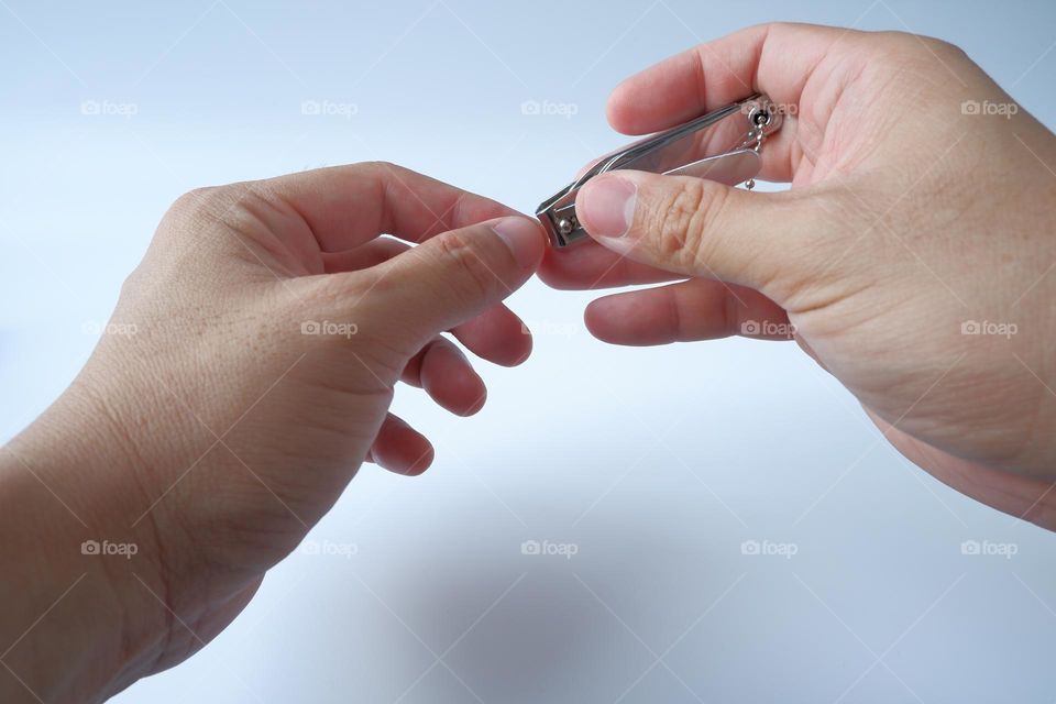 Man cuts his nails with nail clippers on a white background.