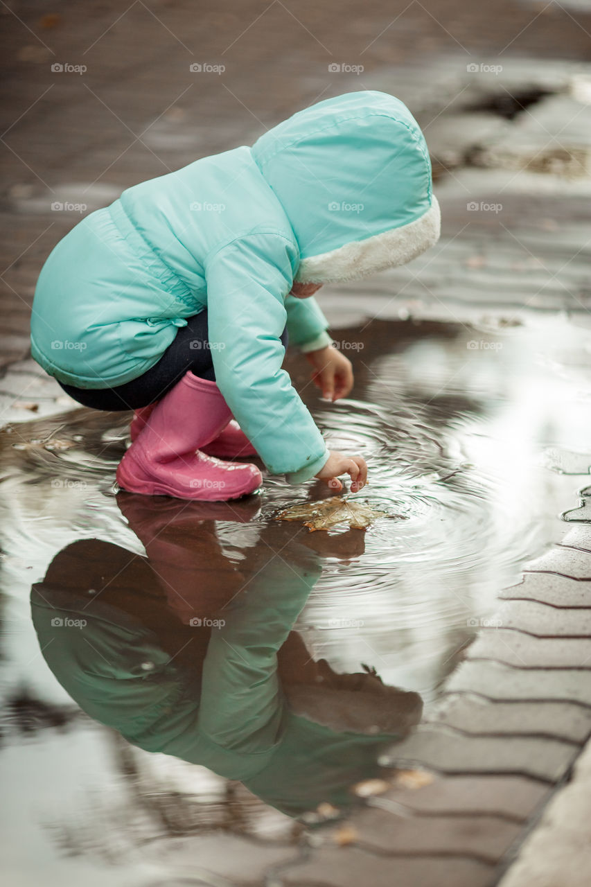 Little girl in rubber boots playing in puddle