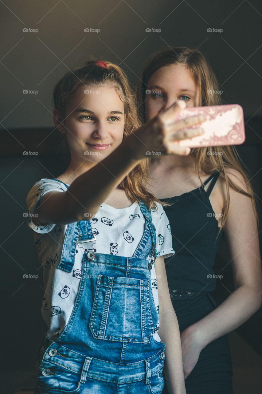 Young women taking selfie, using smartphone camera. Girls making faces, enjoying taking funny pictures together