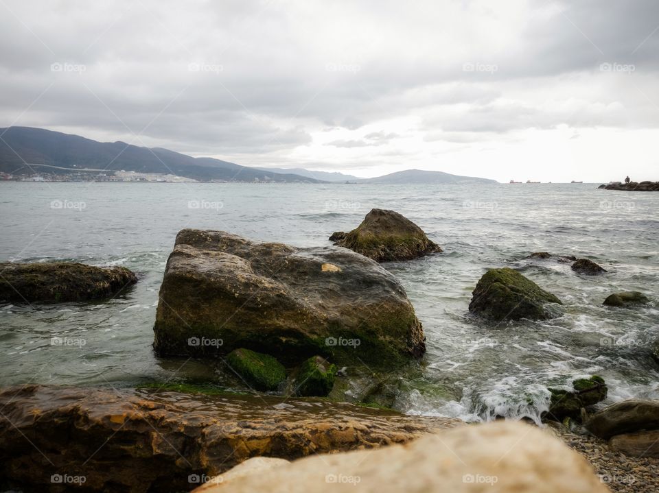 Stones overgrown with algae. It's raining. The waves of the sea. Mountains.