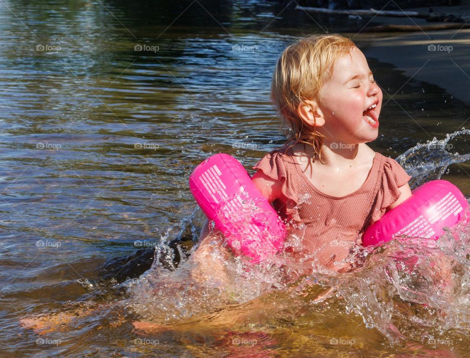 Little girl having fun at the beach and into the water . She is trilled about the water and the fun and the sun and sand .