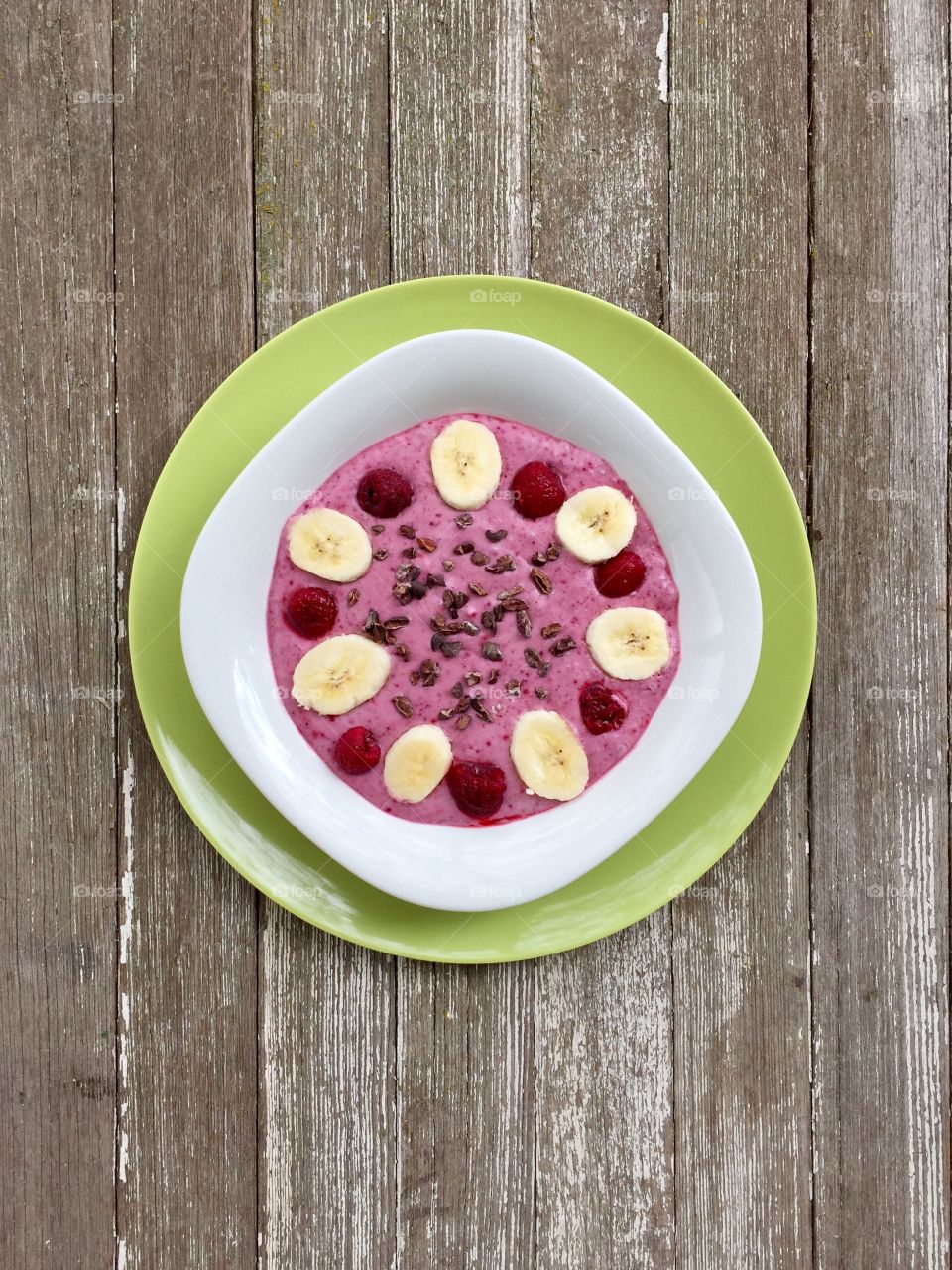 Fruits! - smoothie bowl made with raspberry, banana and  coconut milk, topped with cacao nibs and fresh fruit, in white bowl on green plate, weathered wood surface