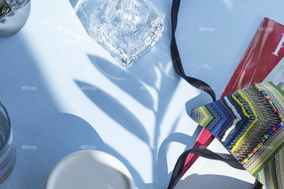 Items and image are selected and prepared for travel. A blue shirt, a glass of clean water and sunglasses, reading magazines on a blue background.