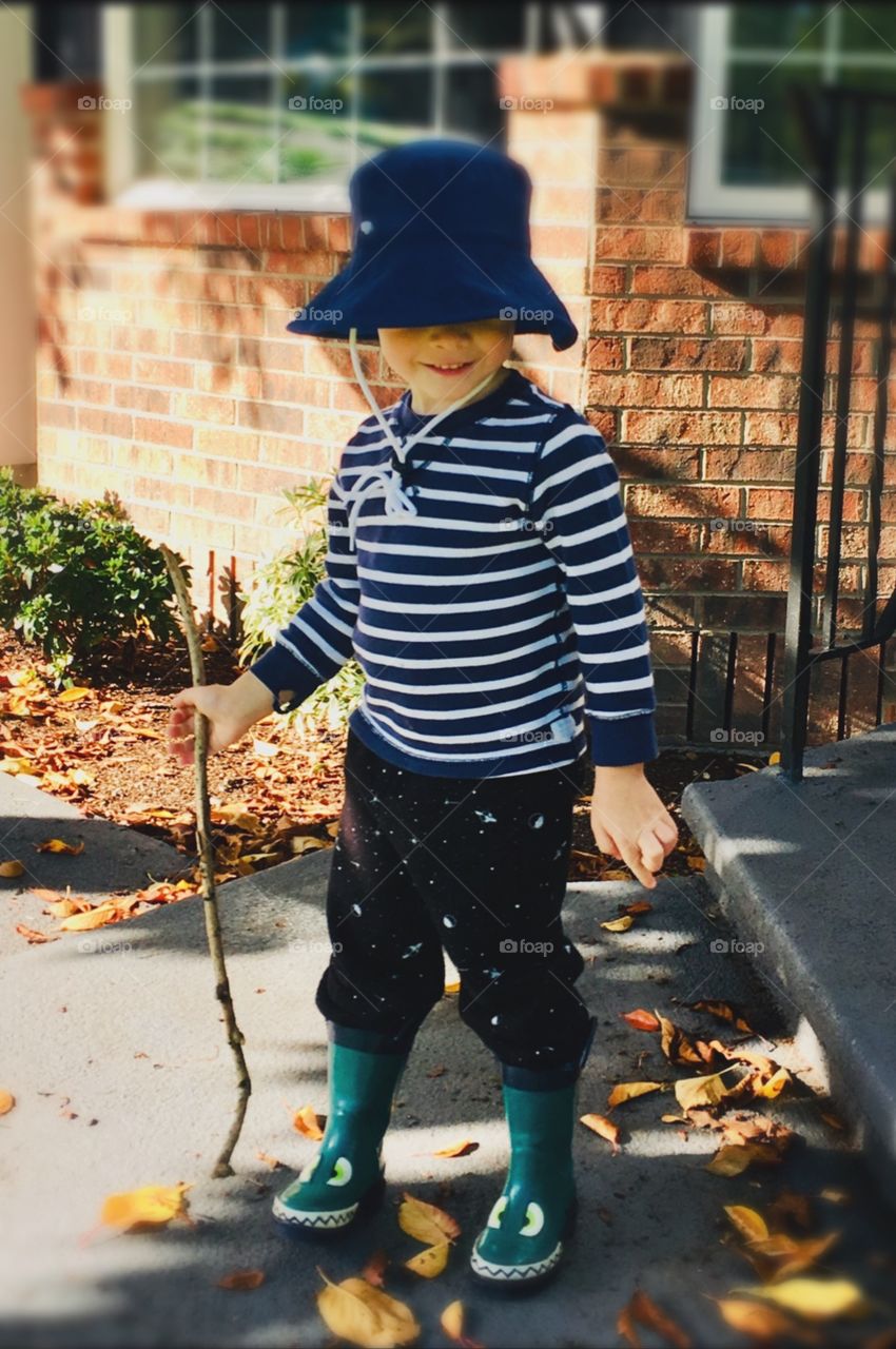 A young child enjoys playing outside with falling leaves on a sidewalk in the fresh air of Autumn 