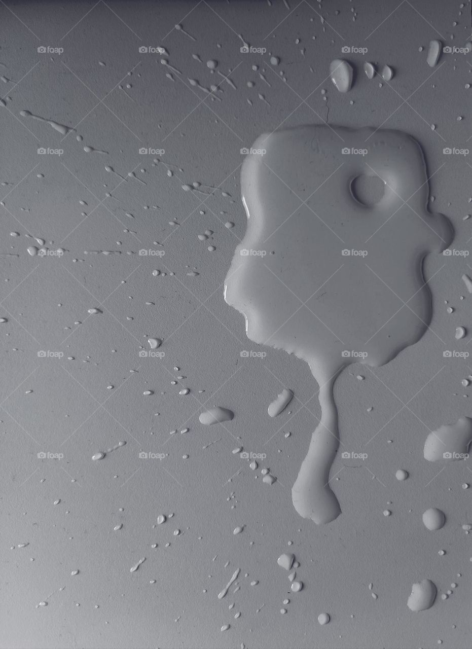 A small water puddle on a white desk shaped as a face with a heart shape in it