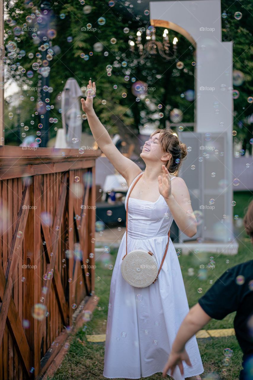 Girl in a white dress catches soap bubbles
