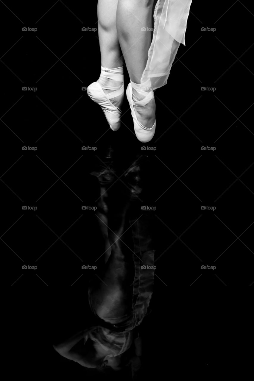 Ballerina dancer on toes, ballet shoes with reflection on black mirror surface. Monochrome black and white image showing beauty and strength.