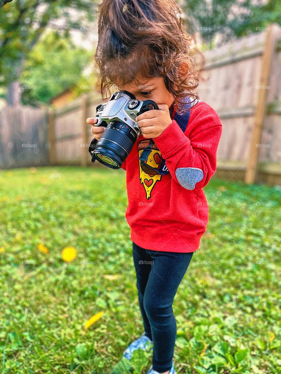 Toddler girl points camera at the ground, focusing on fall leaves, toddler uses film camera, toddlers and cameras, Canon cameras and toddler, toddler photographer, still learning