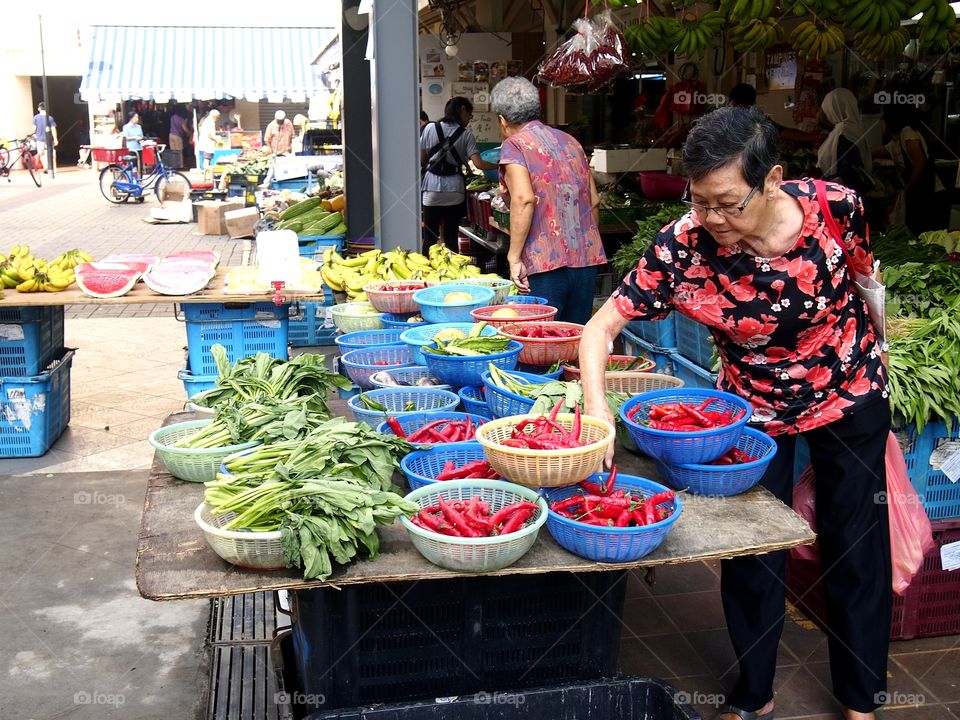 a lady buying fruits and vegetables at a market