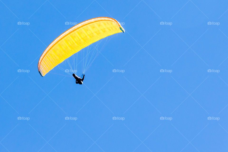Hang glider with bright yellow parachute , clear blue sky in the background 